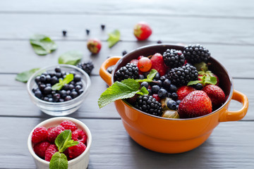 Berries in bowls on wooden background. Composition of raspberry, currant, strawberry, blueberries, gooseberries, blackberries and mint. Health, Diet, Gardening. Harvest Concept