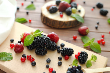 Mix of fresh berries on wooden background. Composition of currant, strawberry, blueberries, gooseberries, blackberries and mint.
