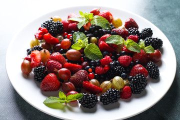 Fruit salad with raspberry, currant, strawberry, blueberries, gooseberries, blackberries and mint on a white plate.