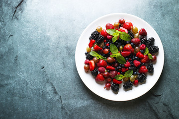 Fruit salad with raspberry, currant, strawberry, blueberries, gooseberries, blackberries and mint on dark background  with space for text. Top view.