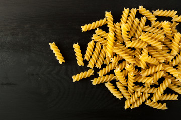 farfalle Raw Fusilli italian pasta on a wood black textured background. Close-up view from the top. Free space for text. - obrazy, fototapety, plakaty