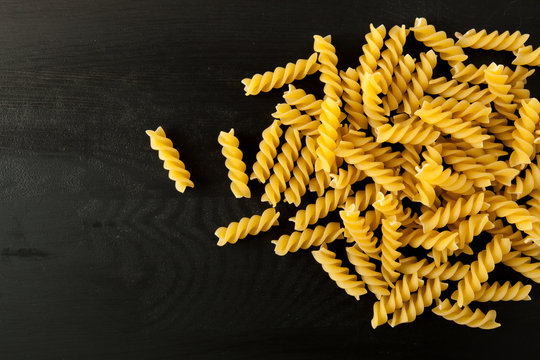 farfalle Raw Fusilli italian pasta on a wood black textured background. Close-up view from the top. Free space for text.