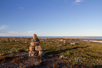 Inukshuk or Inuksuk on a rocky tundra with water in the background in late June in the arctic...