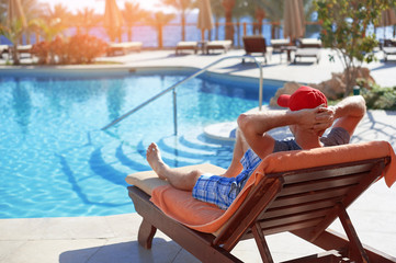 Positive man in red hat resting near the swimming pool hotel in Egypt. Concept beautiful lifestyle