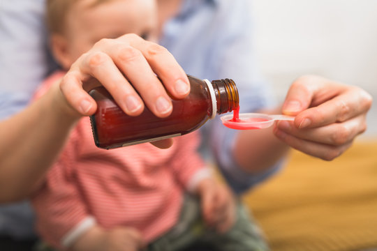 close up of mother pouring cough syrup. blurred baby boy in background