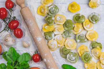 Fototapeta na wymiar Homemade fresh Italian ravioli pasta on white wood table with flour, basil, tomatoes,background,top view.