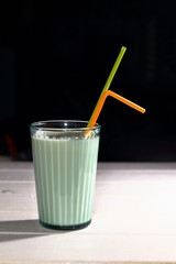 A glass of milk in a transparent faceted glass cupwith straw on a black background