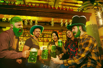 Obraz na płótnie Canvas Saint Patrick's Day Party. Happy friends are celebrating and drinking green beer. Young men and women wearing green hats. Pub Interior.
