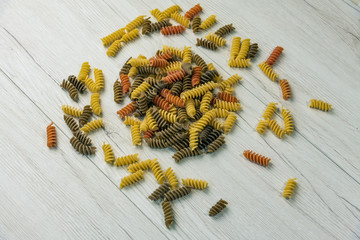 Raw uncooked three-colored Fusilli  on white wood table.