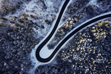 Aerial drone view of a curved winding road through the forest high up in the mountains in the winter with snow covered trees and curved streets in winter