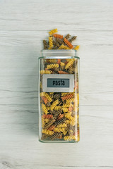 Raw uncooked three-colored Fusilli  in a glass jar on white wood table.
