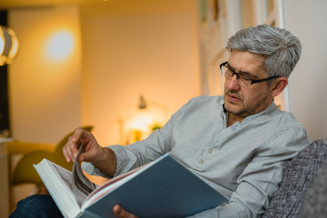 middle aged man reading book relaxed at his sofa