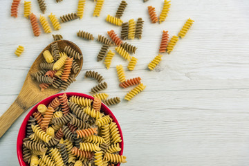 Fototapeta premium Raw uncooked three-colored Fusilli on white wood table.