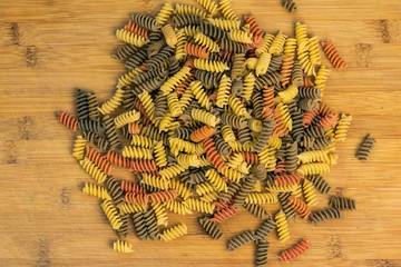 Raw uncooked three-colored Fusilli in on wood table.