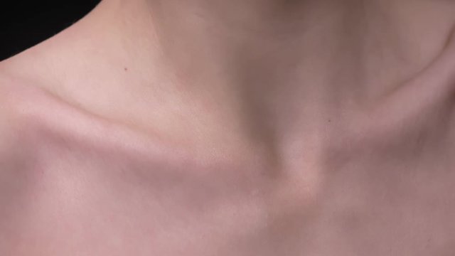 Close-up portrait of skinny caucasian girl moving and showing her collarbone and shoulders on black background.