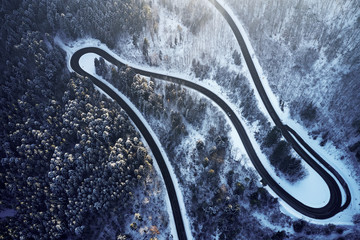 Aerial drone view of a curved winding road through the forest high up in the mountains in the winter with snow covered trees and curved streets in winter