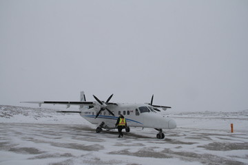 A small plane found on a tarmac in the late morning with snow on the ground being readied for takeoff in a remote northern community