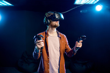 Man playing game using virtual reality headset and gamepads in the dark room of the playing club