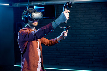 Man playing game using virtual reality headset and gamepads in the dark room of the playing club