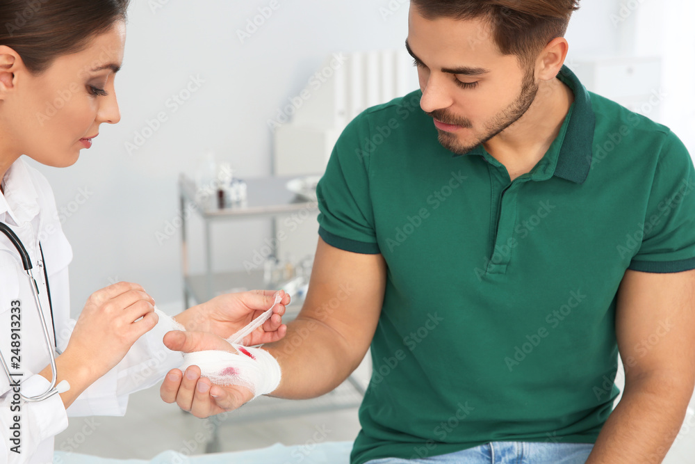 Wall mural Female doctor applying bandage on young man's hand in clinic. First aid