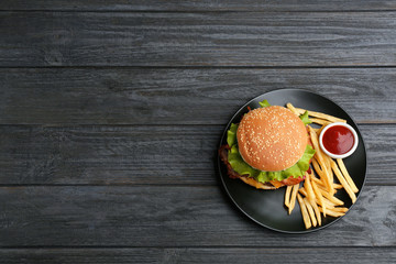 Plate with tasty burger, french fries and sauce on wooden background, top view. Space for text