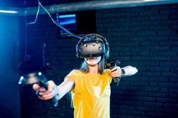 Young woman playing game using virtual reality headset and gamepads in the dark room of the playing club © rh2010