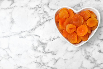 Heart shaped bowl of apricots on marble background, top view with space for text. Dried fruit as healthy food