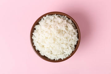 Bowl of boiled rice on color background, top view