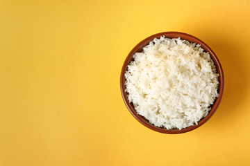 Bowl of boiled rice on color background, top view with space for text