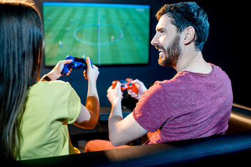 Young excited couple playing football game with gaming console sitting on the couch at the playing...