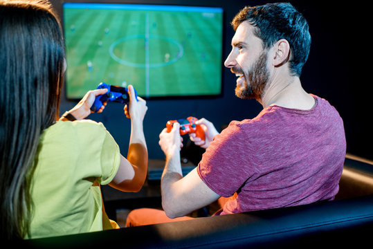 Young excited couple playing football game with gaming console sitting on the couch at the playing club