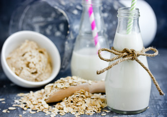 Oat milk in glass jar, homemade oat milk in bottle and raw oat flakes on table, concept of vegetarian and healthy diet