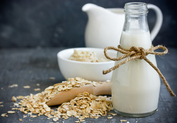 Oat milk in glass jar, homemade oat milk in bottle and raw oat flakes on table, concept of vegetarian and healthy diet