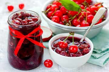 Fototapeta na wymiar Homemade cherry jam in sugar syrup in glass jar on table with fresh cherries in bowl