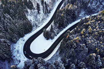 Aerial drone view of a curved winding road through the forest high up in the mountains in the winter with snow covered trees and curved streets in winter