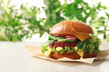 Tasty vegetarian burger with beet cutlet on table against blurred background. Space for text