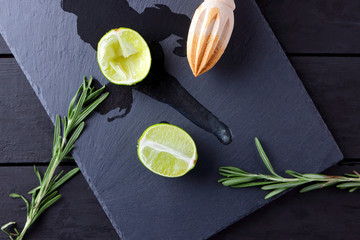 Lime halves and wooden juicer on slate board. Lime and rosemary on black background. Fresh lime juice flows over the stone board. Healthy food