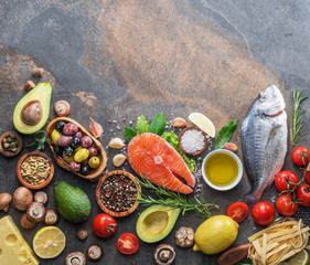 Raw dorado fish and salmon steak with spices and vegetables on the graphite board.