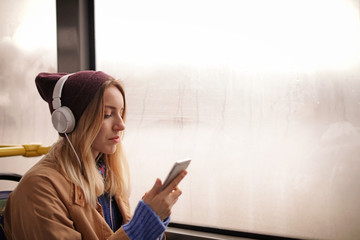 Young woman with headphones listening to music in public transport, space for text