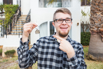 Property, ownership, new home and people concept - young man with keys standing outside new home