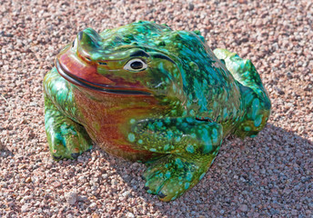 Ceramic frog in green and red colors sitting in the gravel
