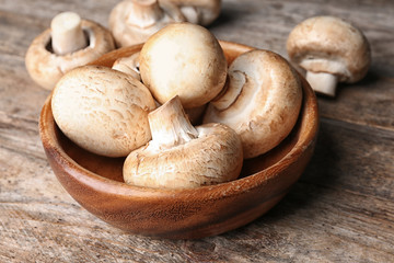 Bowl of fresh champignon mushrooms on wooden table, closeup