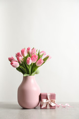 Obraz premium Bouquet of beautiful spring tulips in vase and gift box on table against white background. International Women's Day