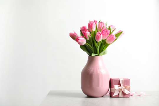 Bouquet of beautiful spring tulips in vase and gift box on table against white background. International Women's Day