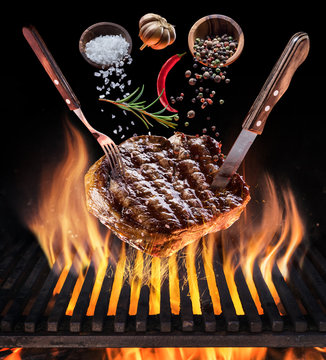 Steak cooking. Conceptual picture. Steak with spices and cutlery under burning grill grate.