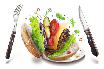 Hamburger ingredients and cutlery hanging in the air. Colorful conceptual picture. Clipping path.