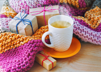 A сup of tea, wrapped gifts and an open book on the background of a knitted blanket.