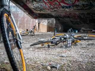 Old yellow scrap bicycles under concrete stairs with graffiti and homeless sleeping shelter