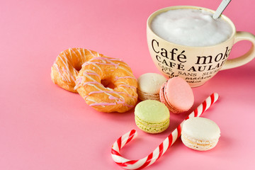 large Cup of cappuccino coffee and donuts and a lot of colorful  French macarons, on the Cup inscription in French (mocha coffee, coffee with milk). pink background, selective focus,without logo