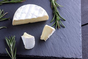 Camembert and rosemary on black stone board. Soft cheese with white mold on black background....